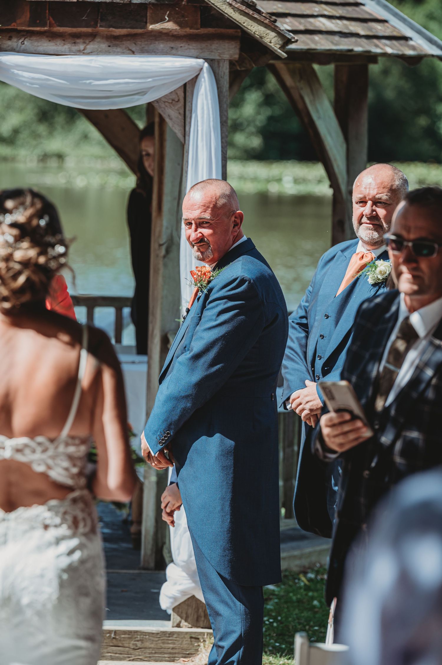 Wedding ceremony taking place at a waterfront gazebo decorated with white fabric draping.