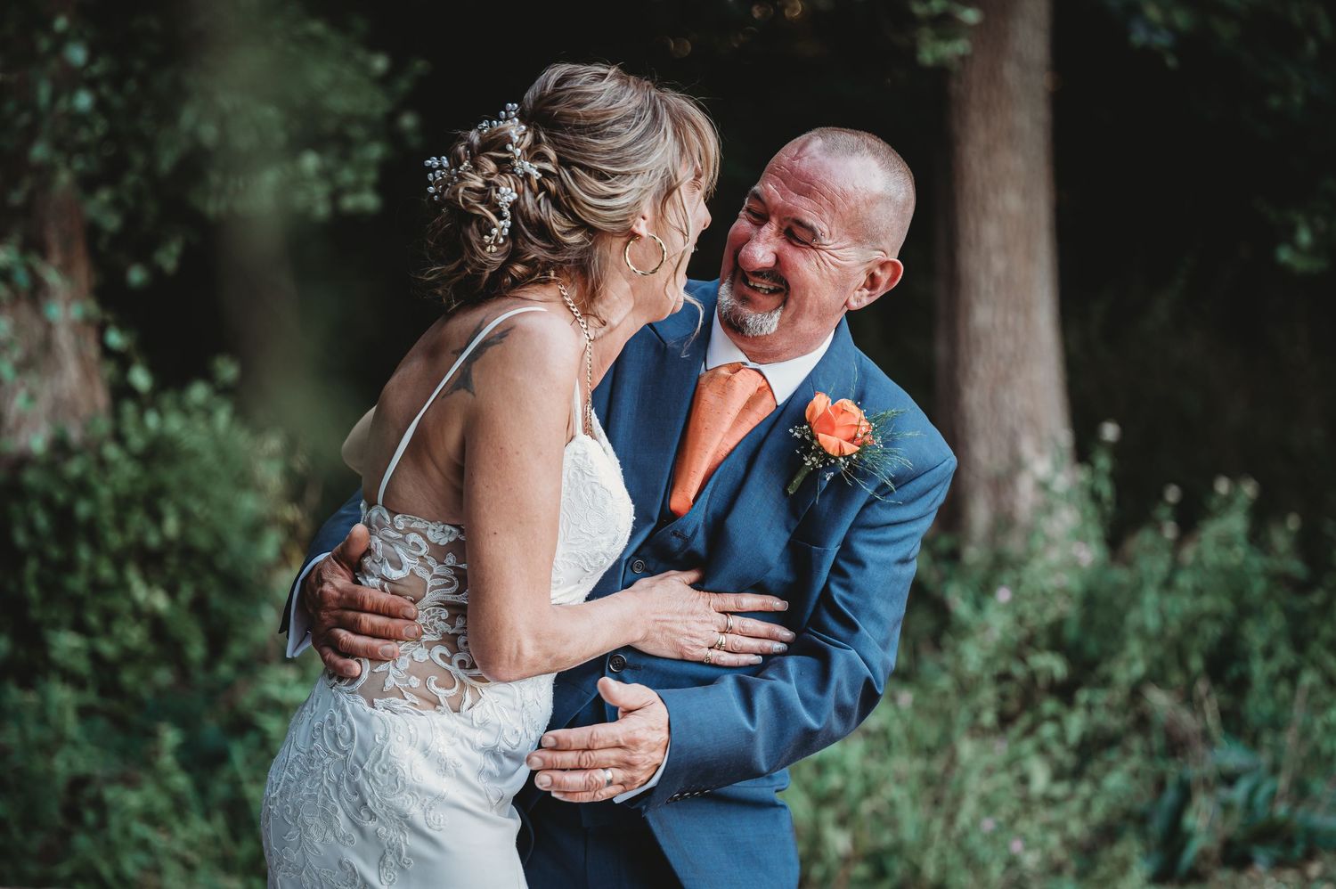 Joyful moment captured during outdoor wedding with bride and groom sharing laughter in a garden setting.