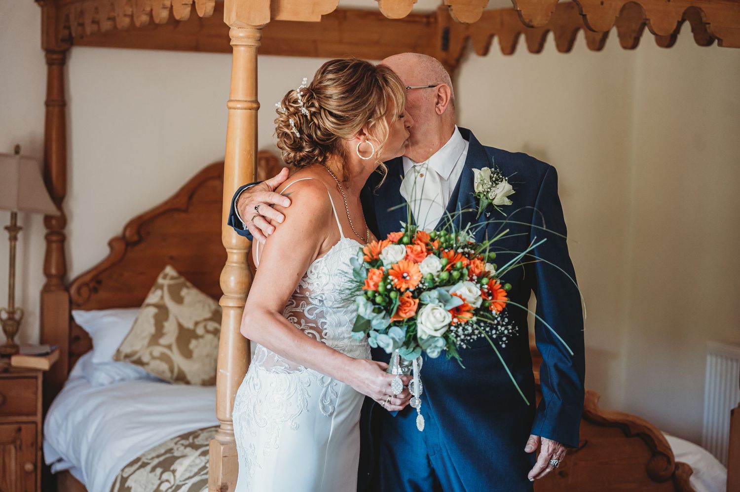 Elegant wedding couple shares an intimate moment with colorful orange and blue floral bouquet in rustic indoor setting.