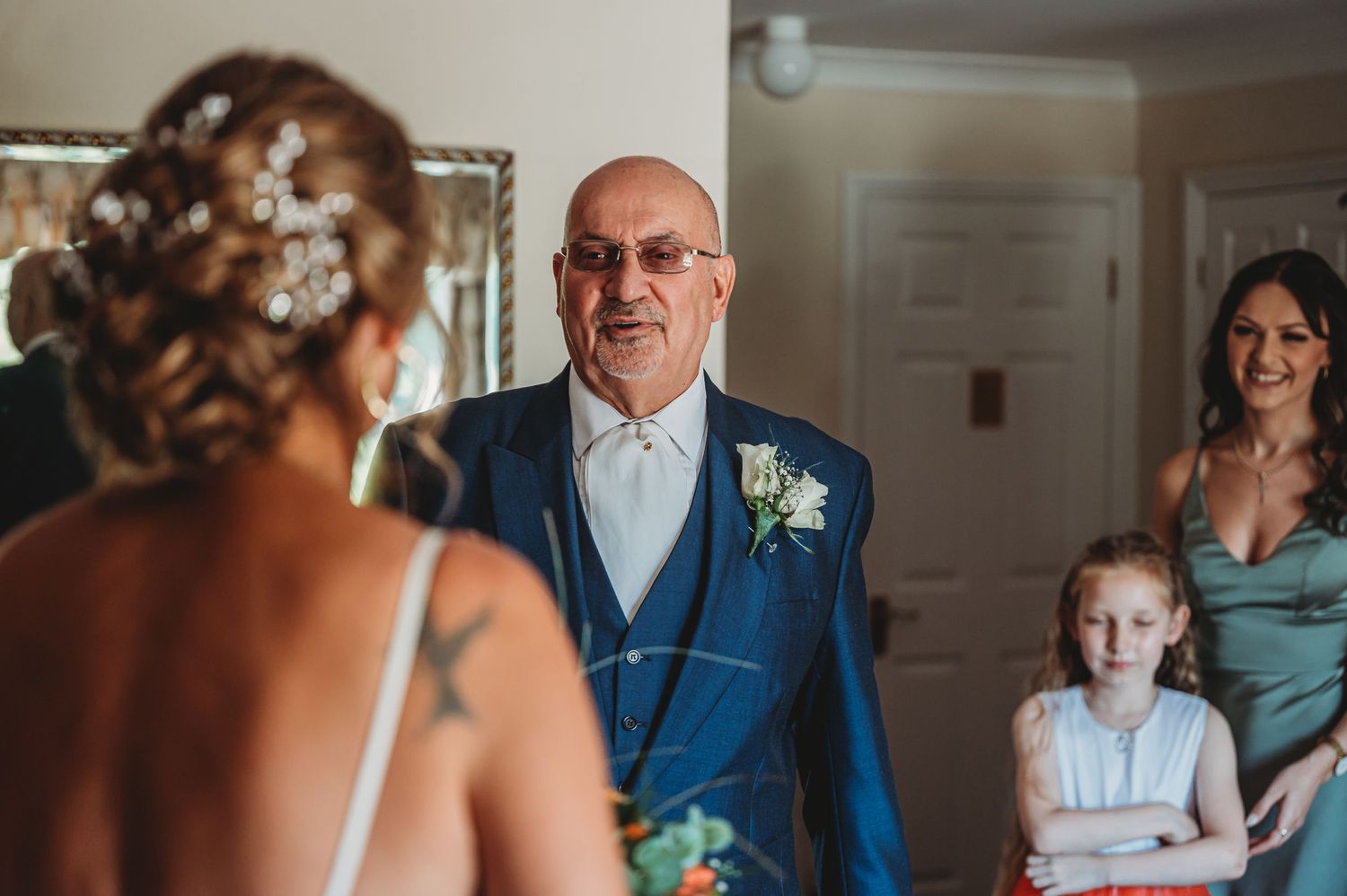 An emotional first look moment at a wedding with someone in a blue suit and white boutonniere reacting to seeing someone special.