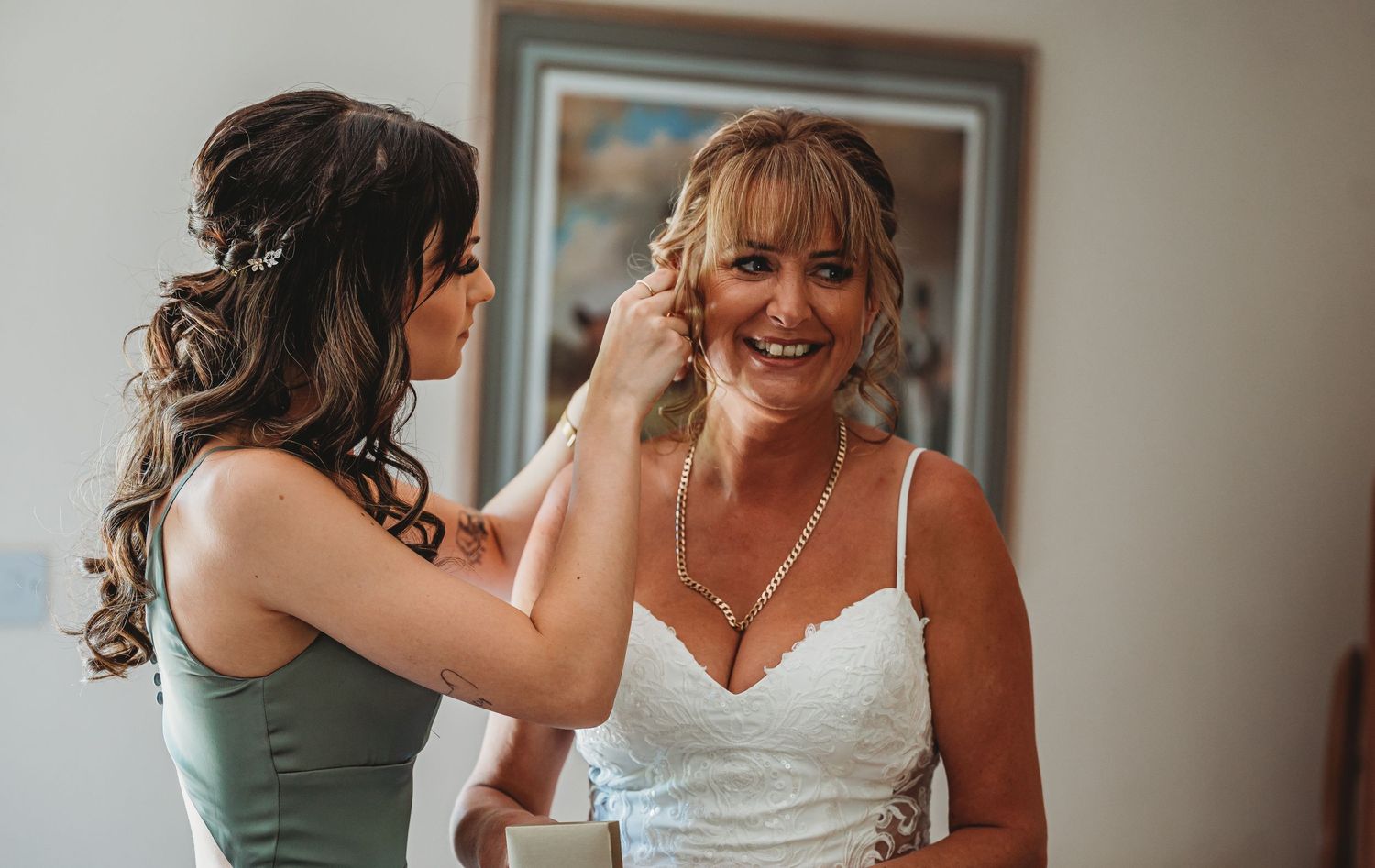 A bride in a white wedding dress smiles as someone helps adjust her hair before the ceremony.