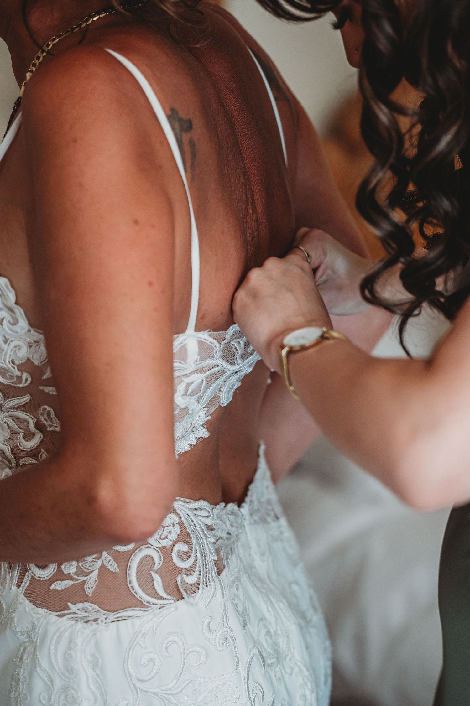 Close-up of delicate white lace detail on a bridal gown being fastened with intricate floral embroidery pattern.