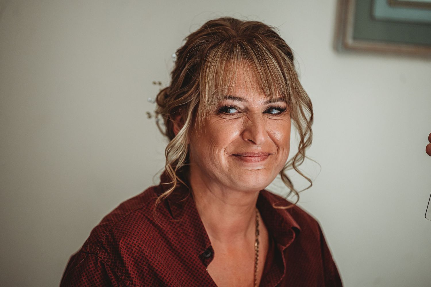 Someone wearing a maroon sweater smiles warmly while sitting against a light colored wall.