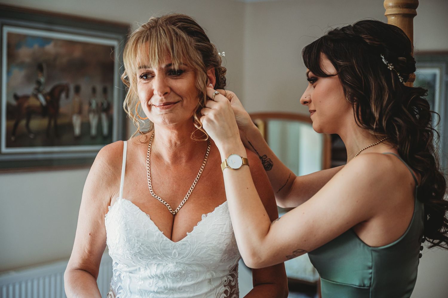 A bridesmaid in a mint green dress helps the bride put on earrings during wedding preparations.