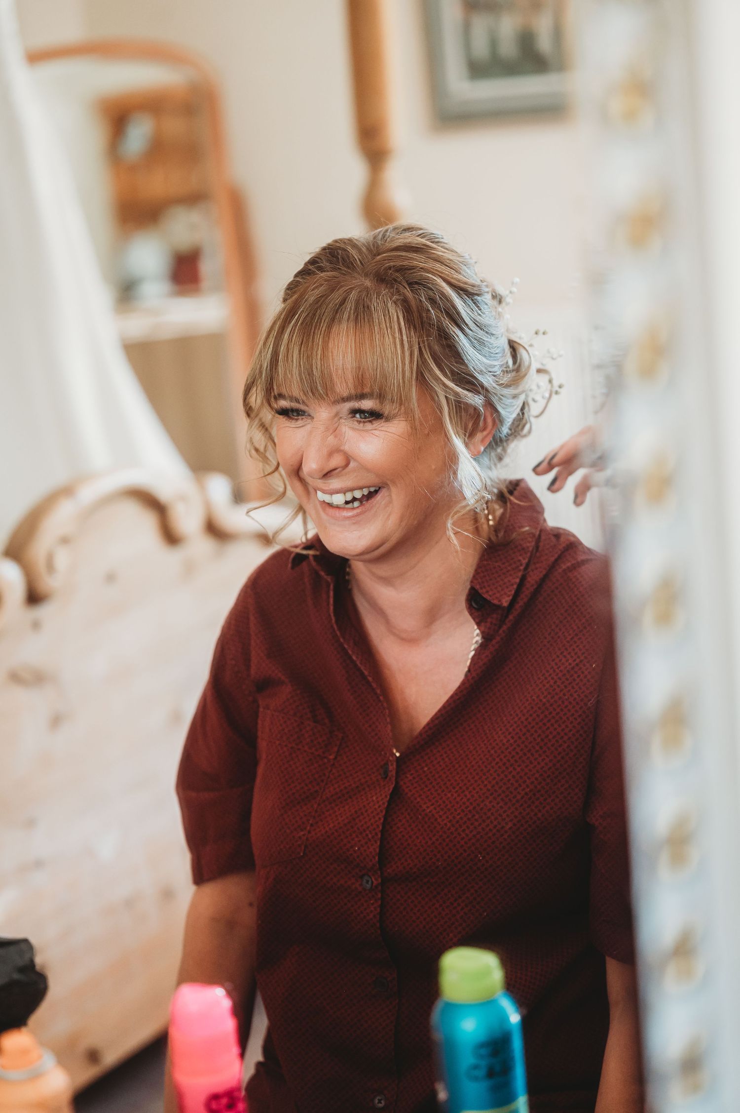 A person wearing a burgundy button-up shirt smiles warmly in a softly lit interior setting.