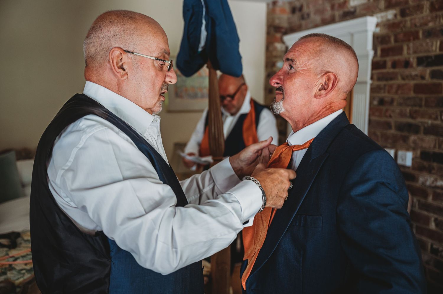 Two people in formal wear help each other with orange neckties while getting dressed for a special occasion.