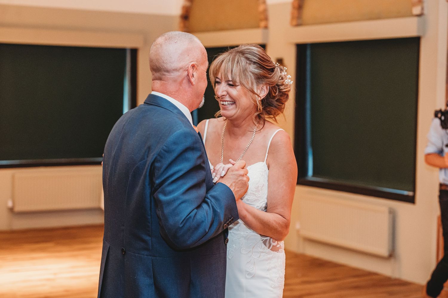 A couple shares their first dance at a wedding reception in a room with wooden floors and green walls.