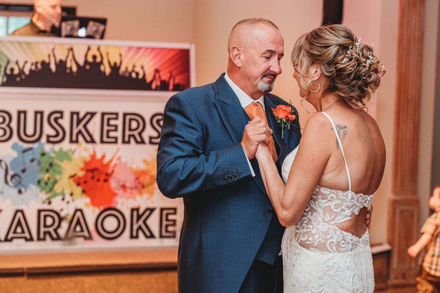 A couple dances at their wedding reception in front of a colorful Buskers Karaoke sign.