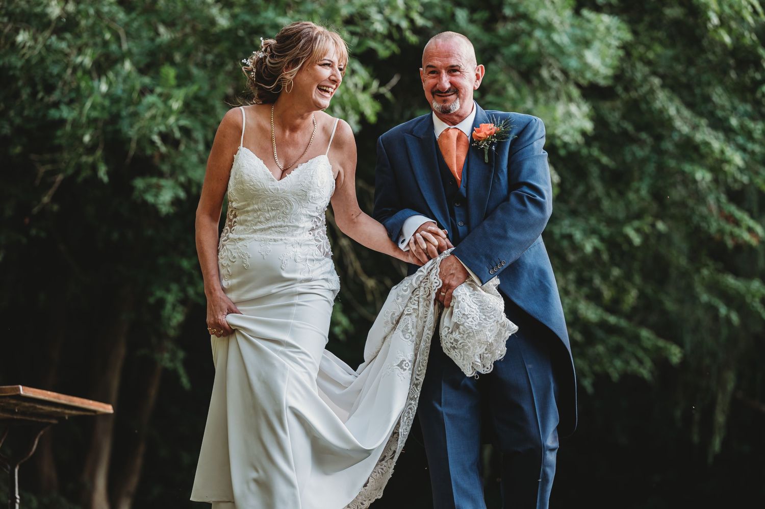 Happy couple laughing and walking together outdoors at their wedding ceremony in formal attire.