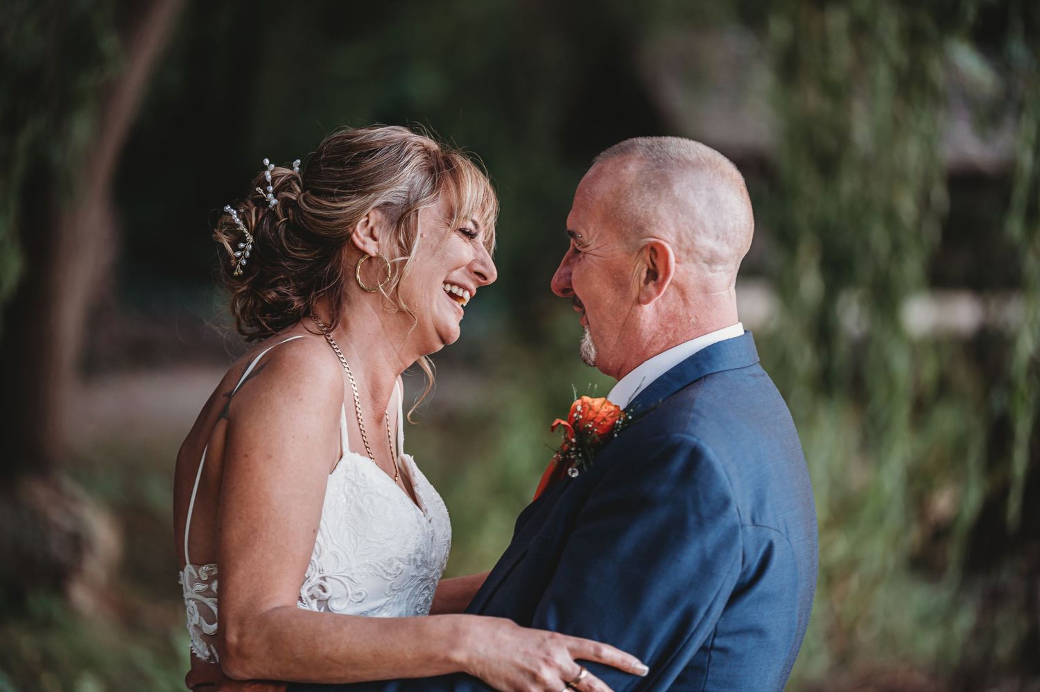 A joyful couple shares an intimate moment together at their wedding, with the bride in white and groom in navy.