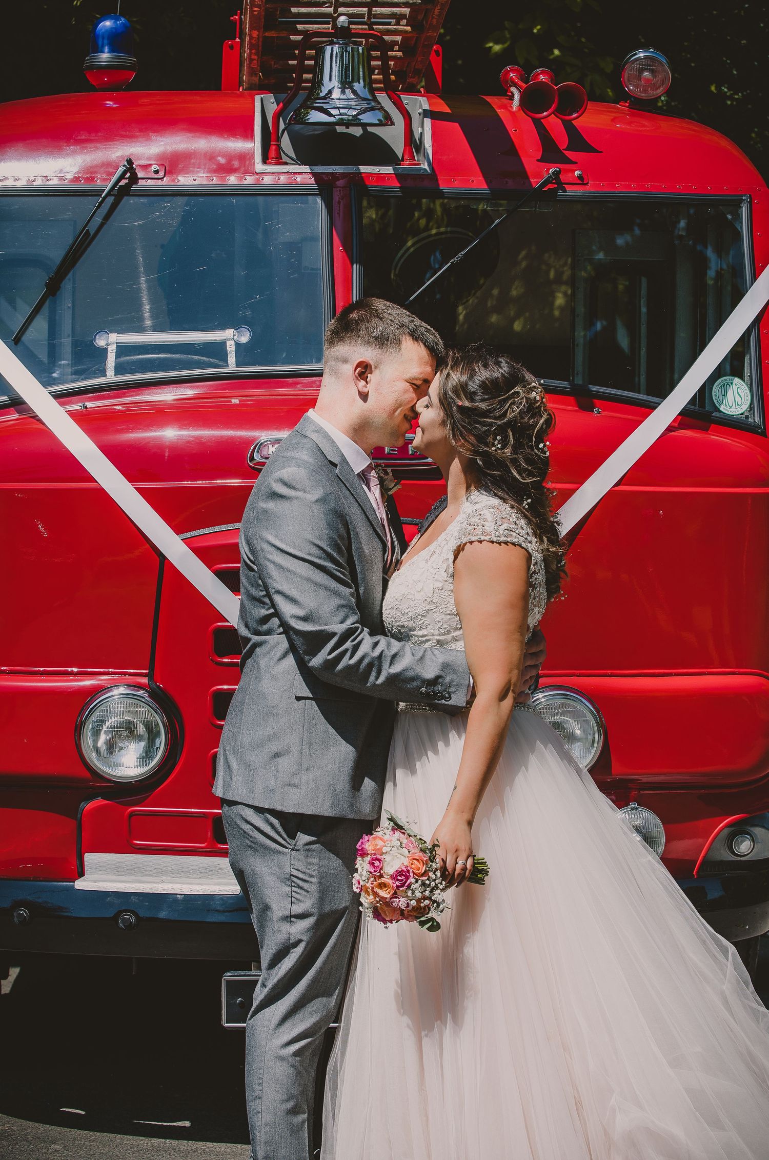 A romantic wedding couple poses in front of a vintage red fire truck during their special day.