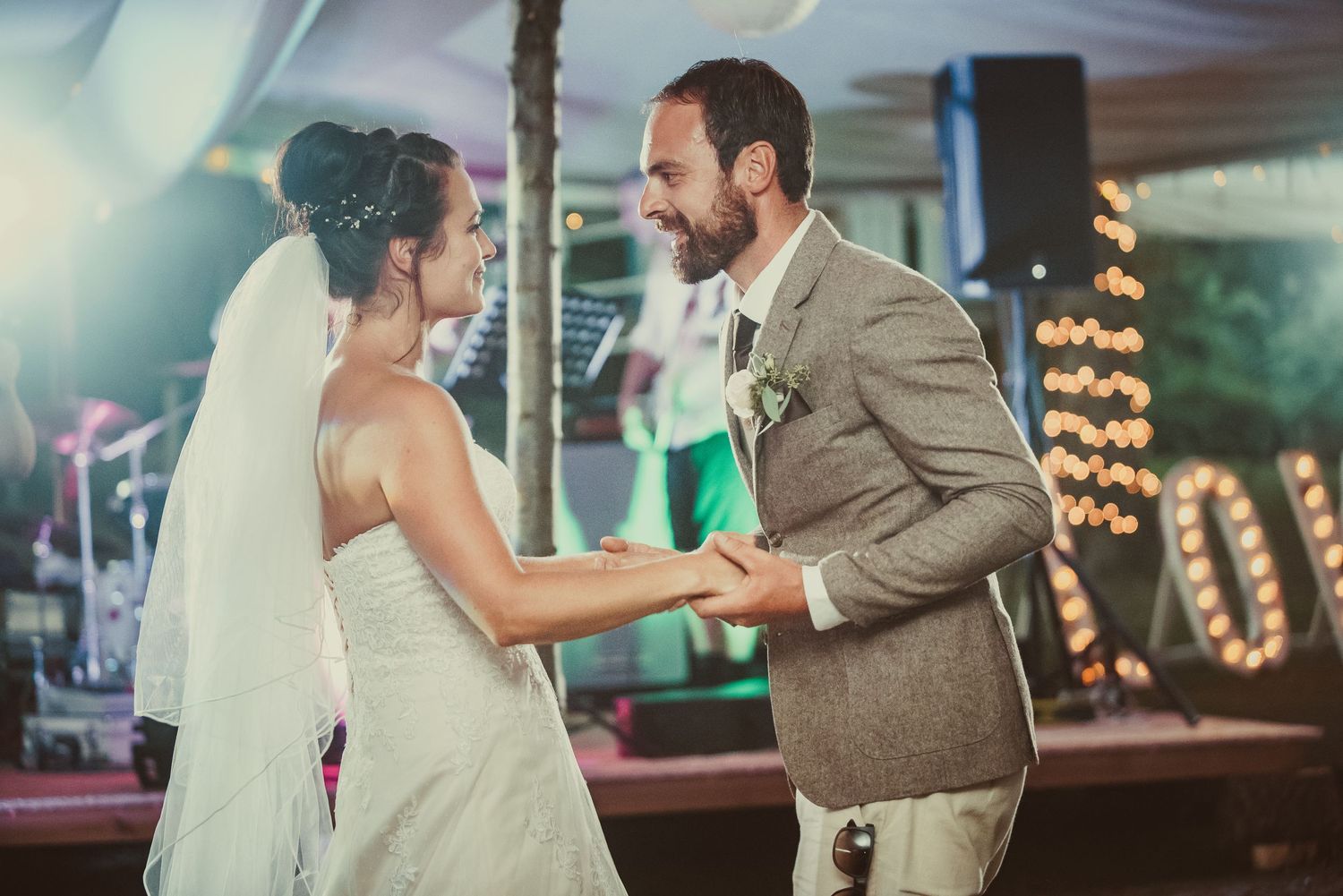 A joyful couple shares their first dance together at an evening wedding reception with twinkling lights in background.