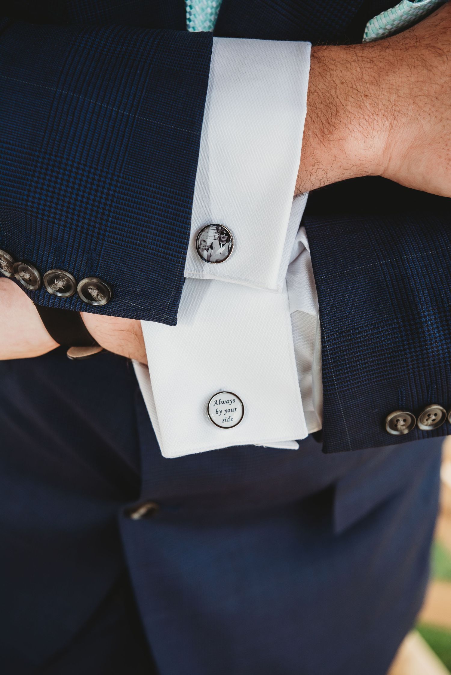 Close-up of a navy suit sleeve with white shirt cuff and decorative silver cufflinks on display.