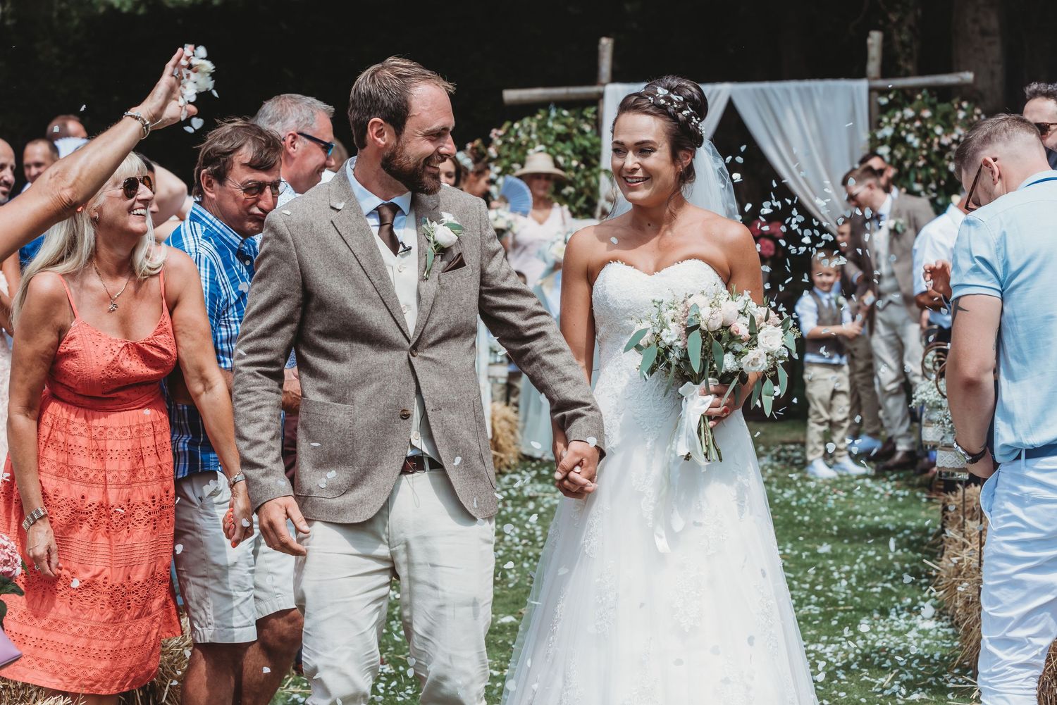 A happy wedding couple walks down the aisle while guests shower them with confetti at an outdoor garden ceremony.