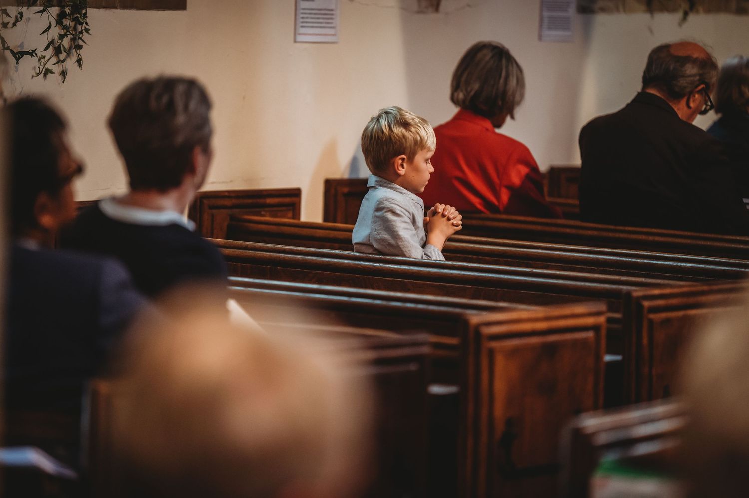 Wooden church pews filled with congregants attending a church service in a bright interior space.