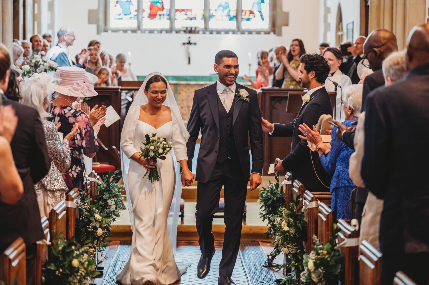 A newly married couple walks down the church aisle while wedding guests cheer and wave during the recessional.