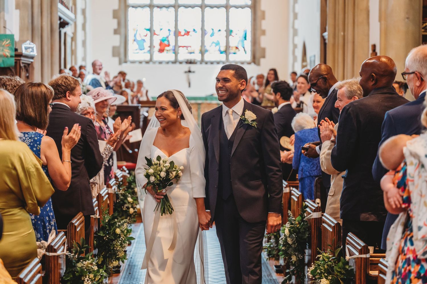 A newlywed couple walks down the church aisle while guests applaud during their wedding ceremony.