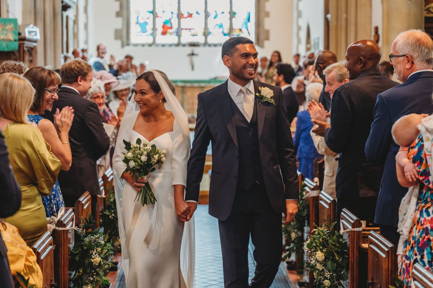 A couple walks down the aisle of a church while wedding guests line the pews during a traditional ceremony.