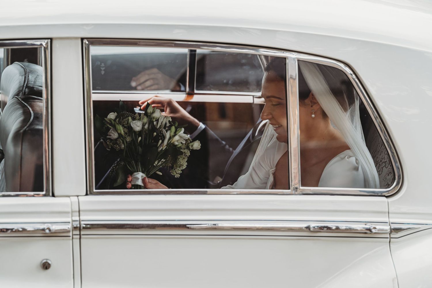 A classic white wedding car with elegant side window showing passenger holding floral bouquet.