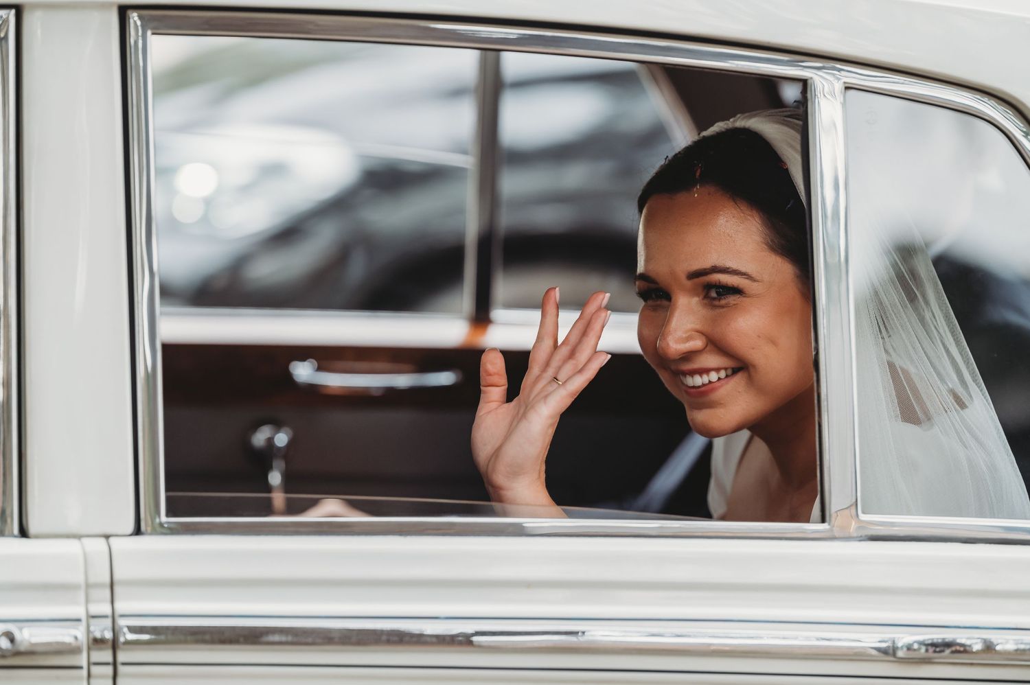 Someone waves through the window of a vintage car with a bright smile on their face.