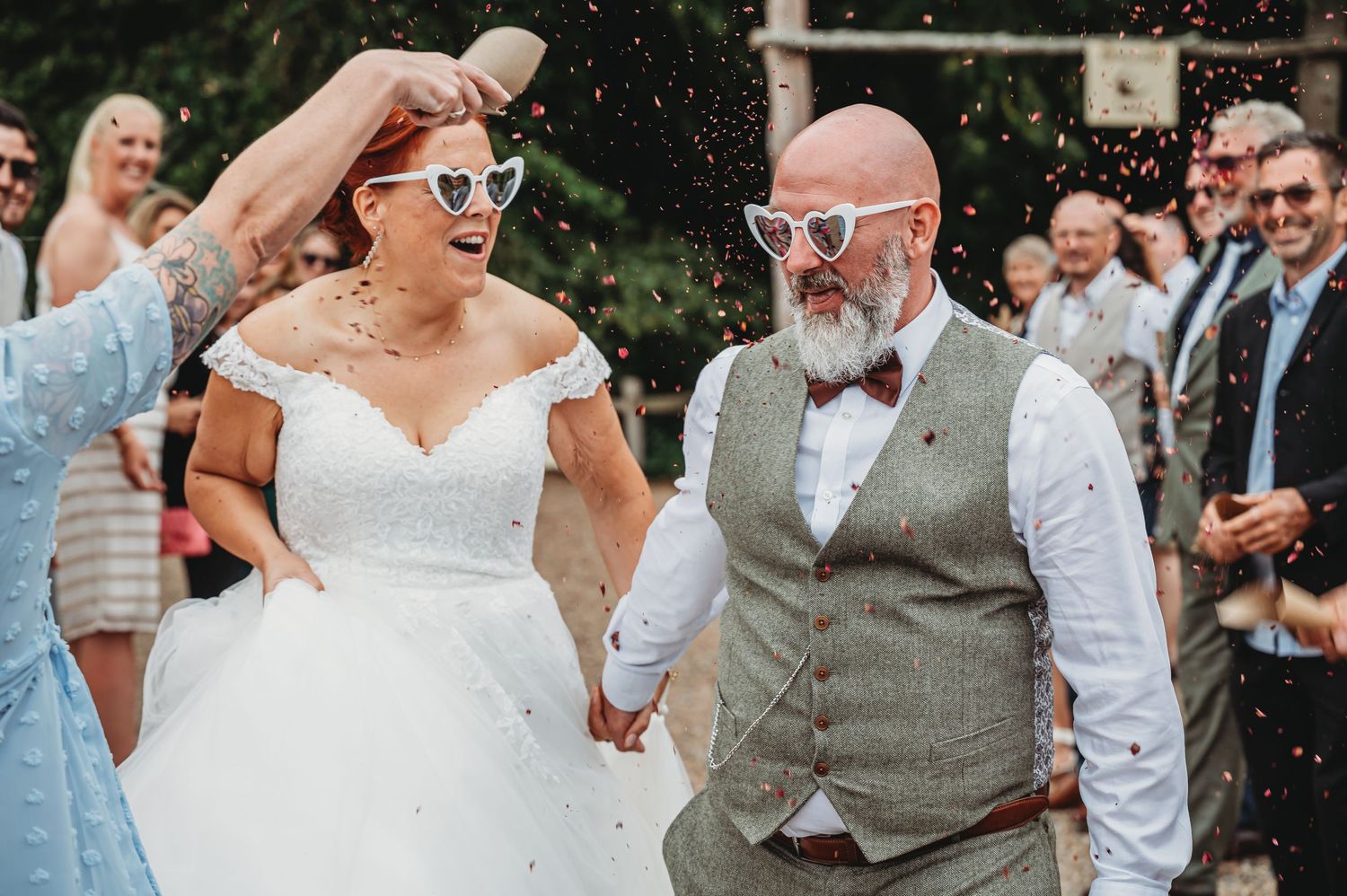 A joyful couple celebrates their wedding day while guests shower them with confetti in an outdoor setting.