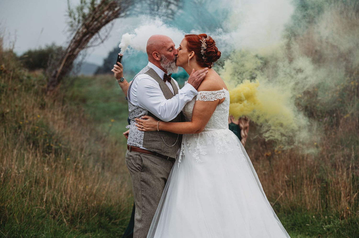 A romantic wedding photo with pastel smoke bombs creating a dreamy atmosphere in a rustic outdoor setting.