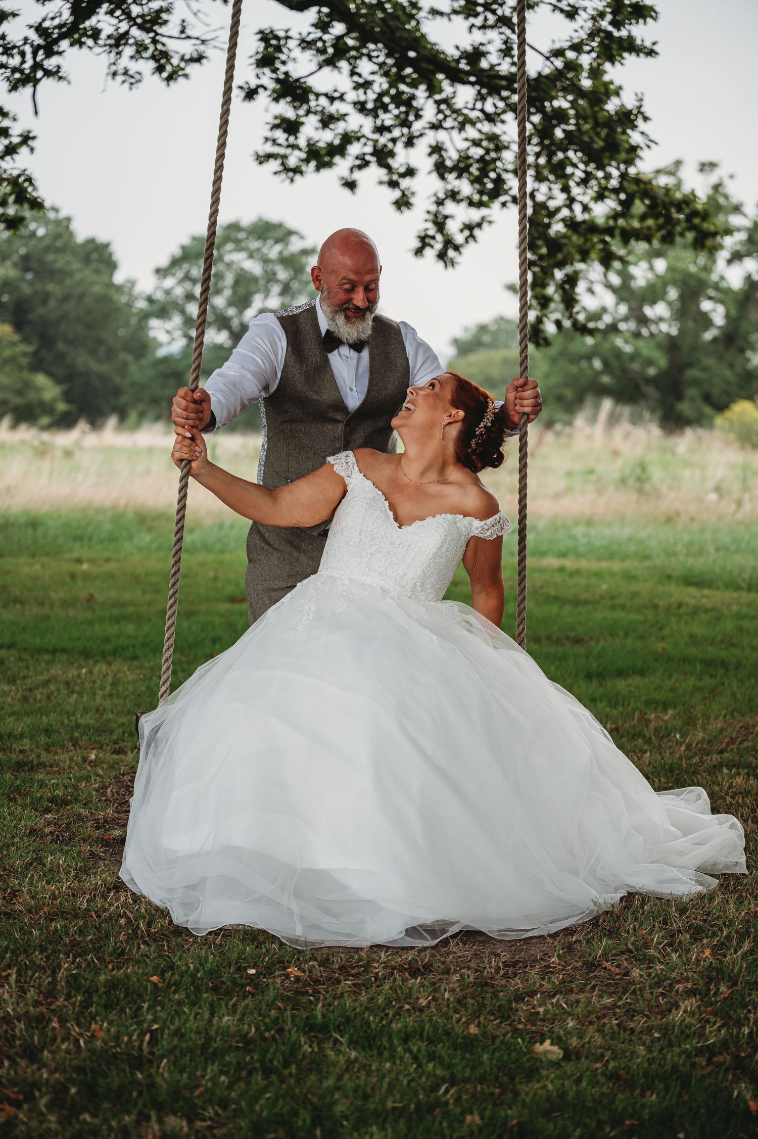 A joyful wedding scene with a couple sharing a playful moment on a rustic rope swing in an outdoor garden setting.