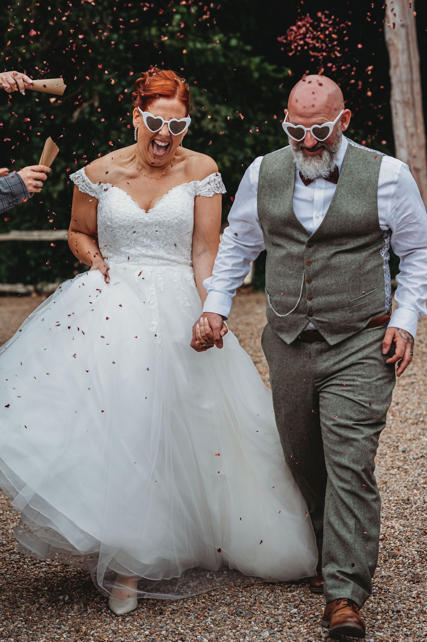 Fun-loving newlyweds wearing sunglasses walk hand in hand as confetti falls around them on their wedding day.