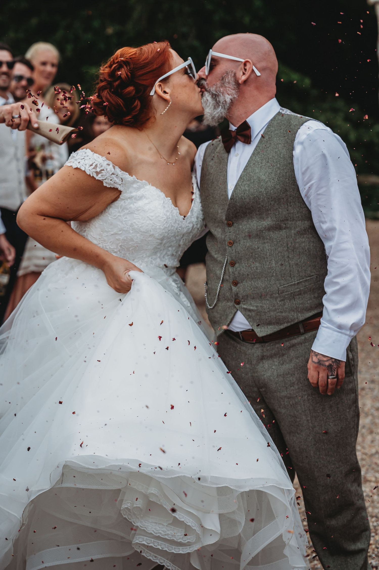 A romantic moment at a wedding ceremony as a couple kisses while confetti falls around them outdoors.