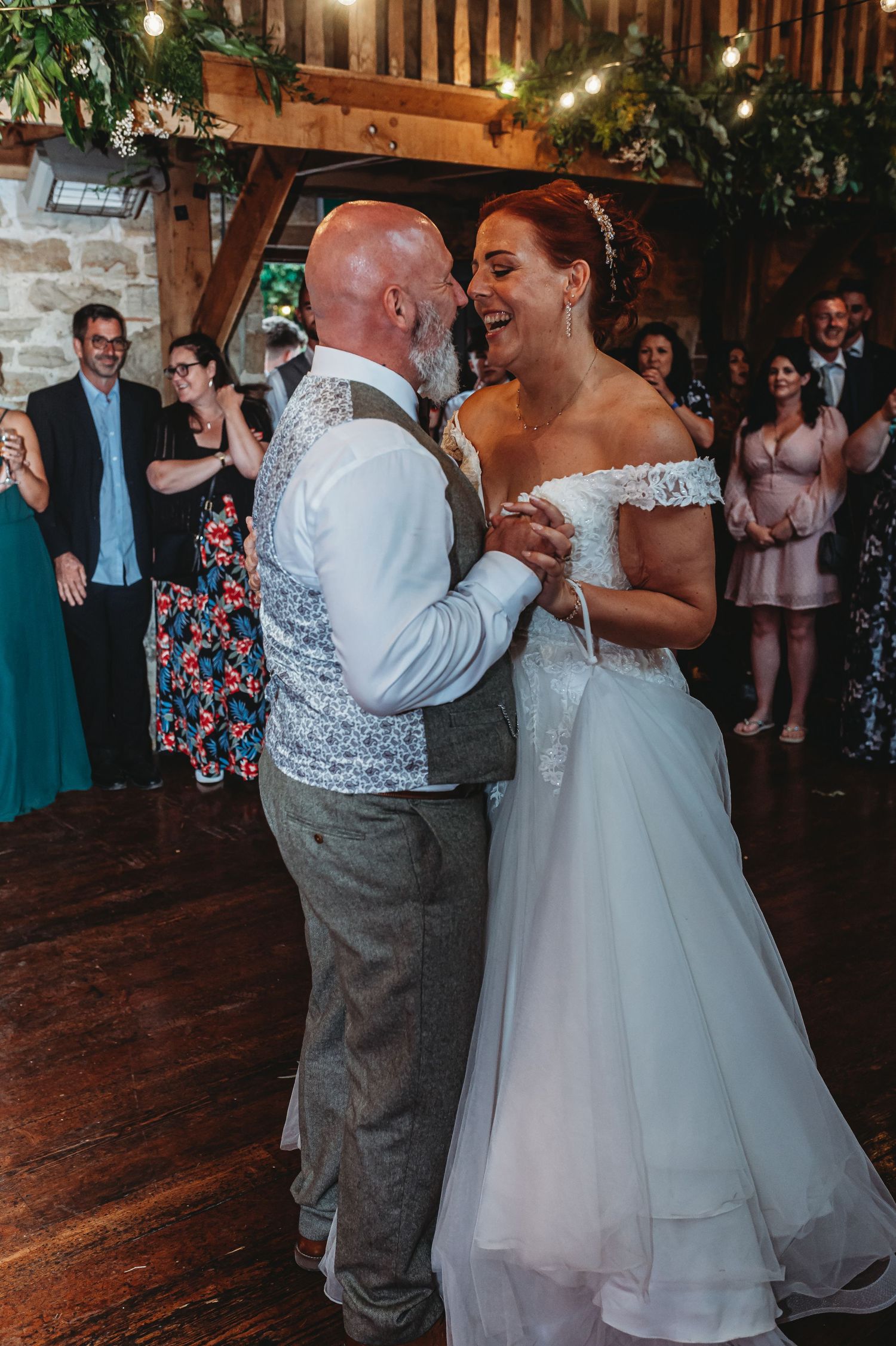 A couple shares their first dance at a rustic wedding reception with string lights and greenery overhead.
