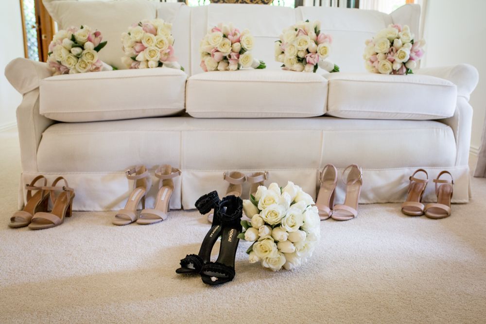 The image shows a white couch with several bouquets of flowers placed on it In front of the couch, there are multiple pairs of shoes arrange