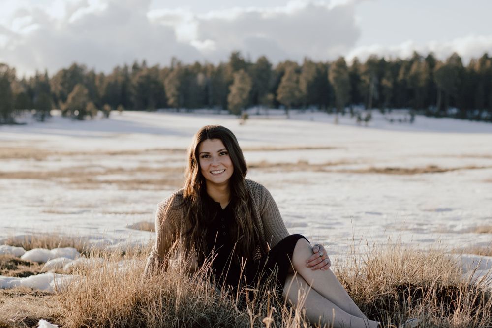 A winter portrait in snowy field with forest backdrop during golden hour.