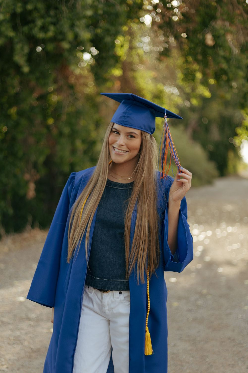 Graduate in blue cap and gown posing outdoors with golden tassel.