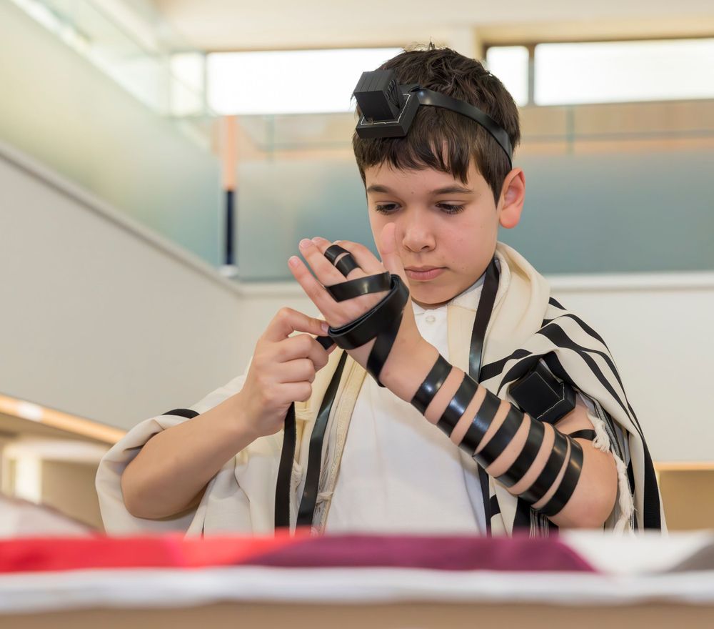 Young person reading from a Torah scroll while wearing traditional prayer shawl in synagogue.