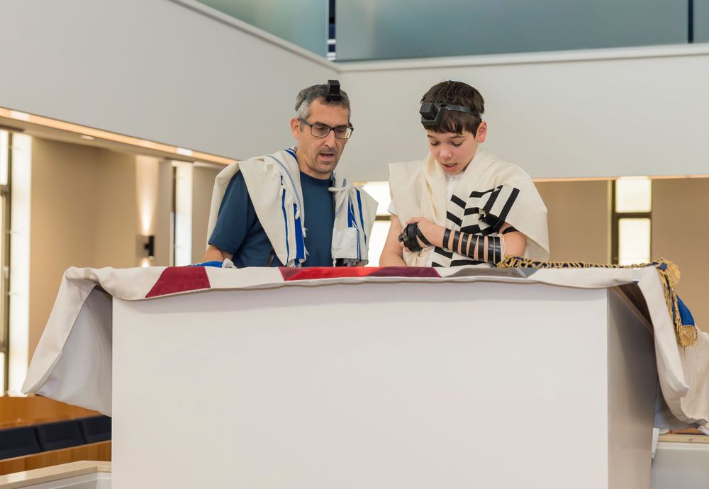 Adult and youth studying religious text together at synagogue podium.