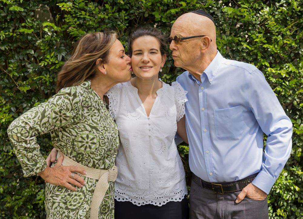 Family members sharing affectionate moment outdoors against green hedge background.