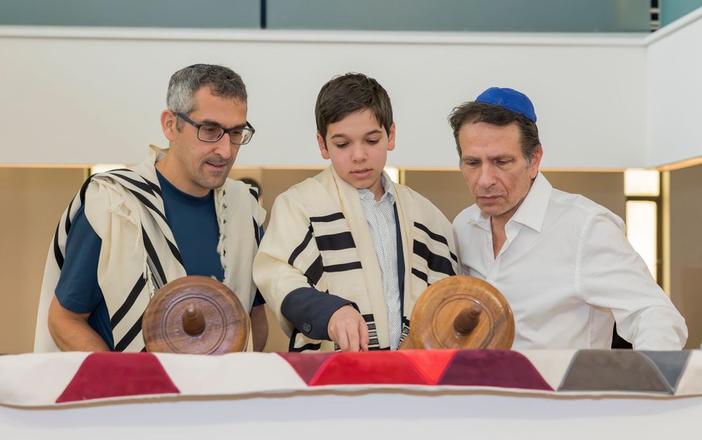Three people examining Torah scroll during religious ceremony.