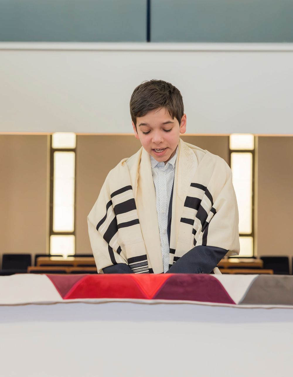 Person wearing prayer shawl reading from Torah scroll during religious ceremony.