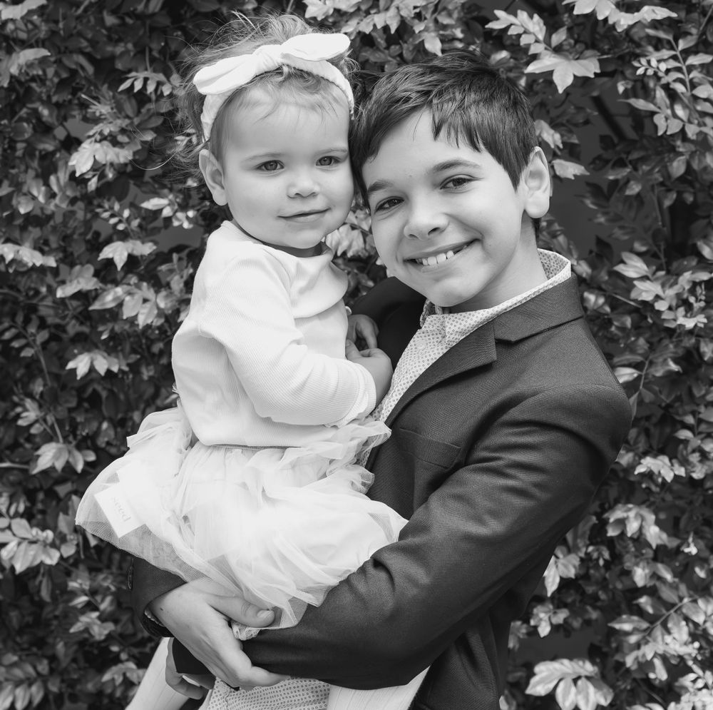 Black and white portrait of siblings posing together against leafy background.