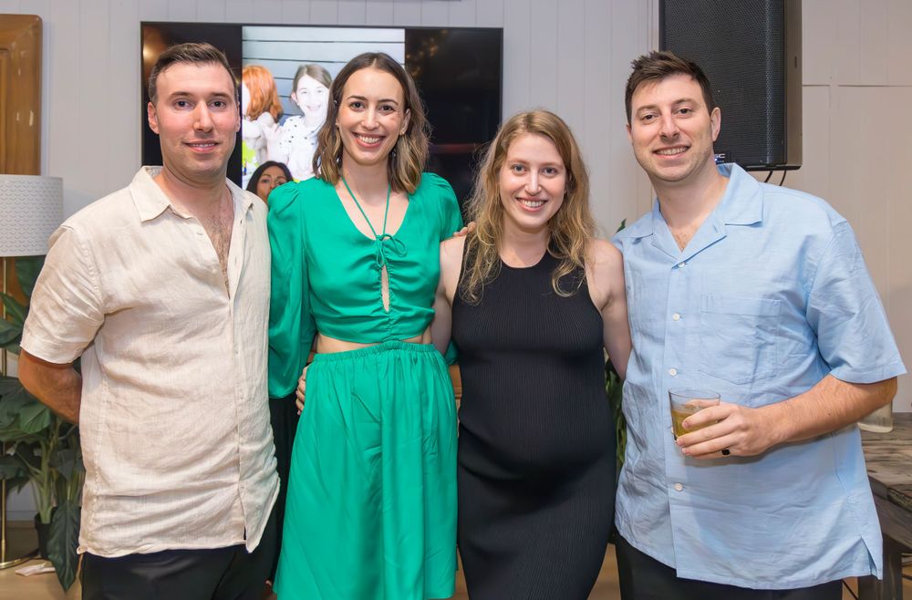 Four friends pose together at a social gathering, with one wearing a striking green dress.