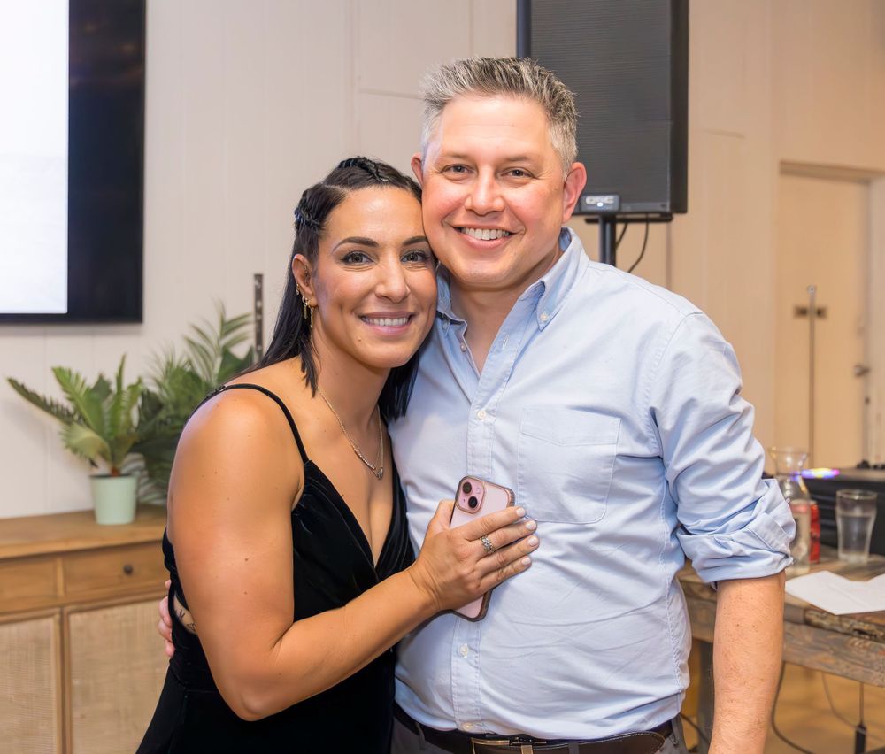 A couple in formal attire poses together at an indoor event space.
