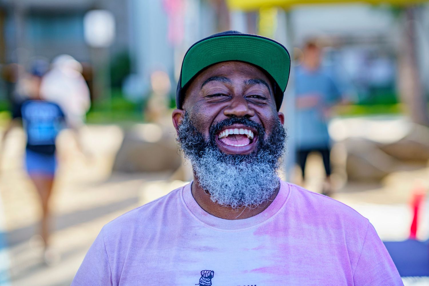 A joyful expression with gray beard wearing a green baseball cap outdoors.