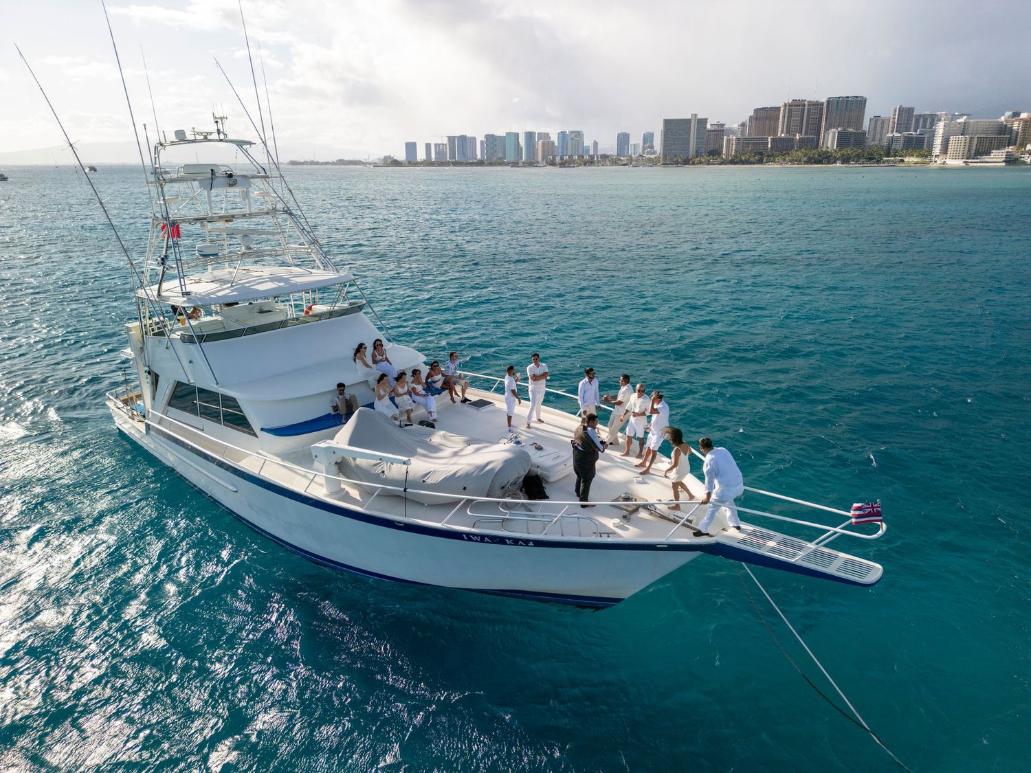 Large fishing yacht sailing in blue ocean waters with Honolulu skyline visible in distance.