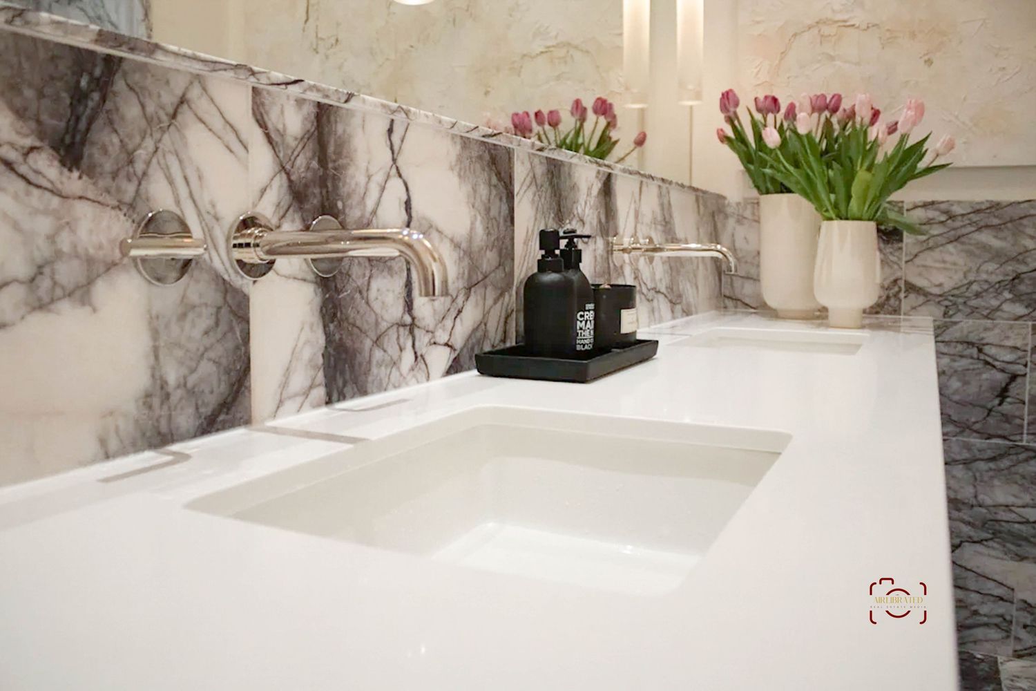 Luxury bathroom vanity with marble backsplash, white countertop, and tulips in a vase.