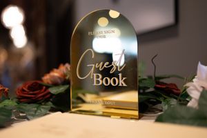 Illuminated gold wedding guest book sign on dark background with rose decoration.