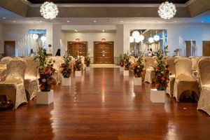 Elegant wedding venue setup with white chairs and floral arrangements along the aisle.