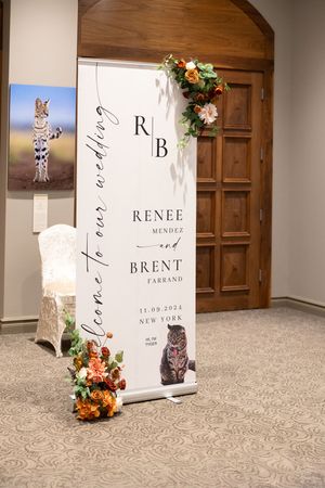 Wedding welcome sign with floral decorations and couple's names displayed on easel.
