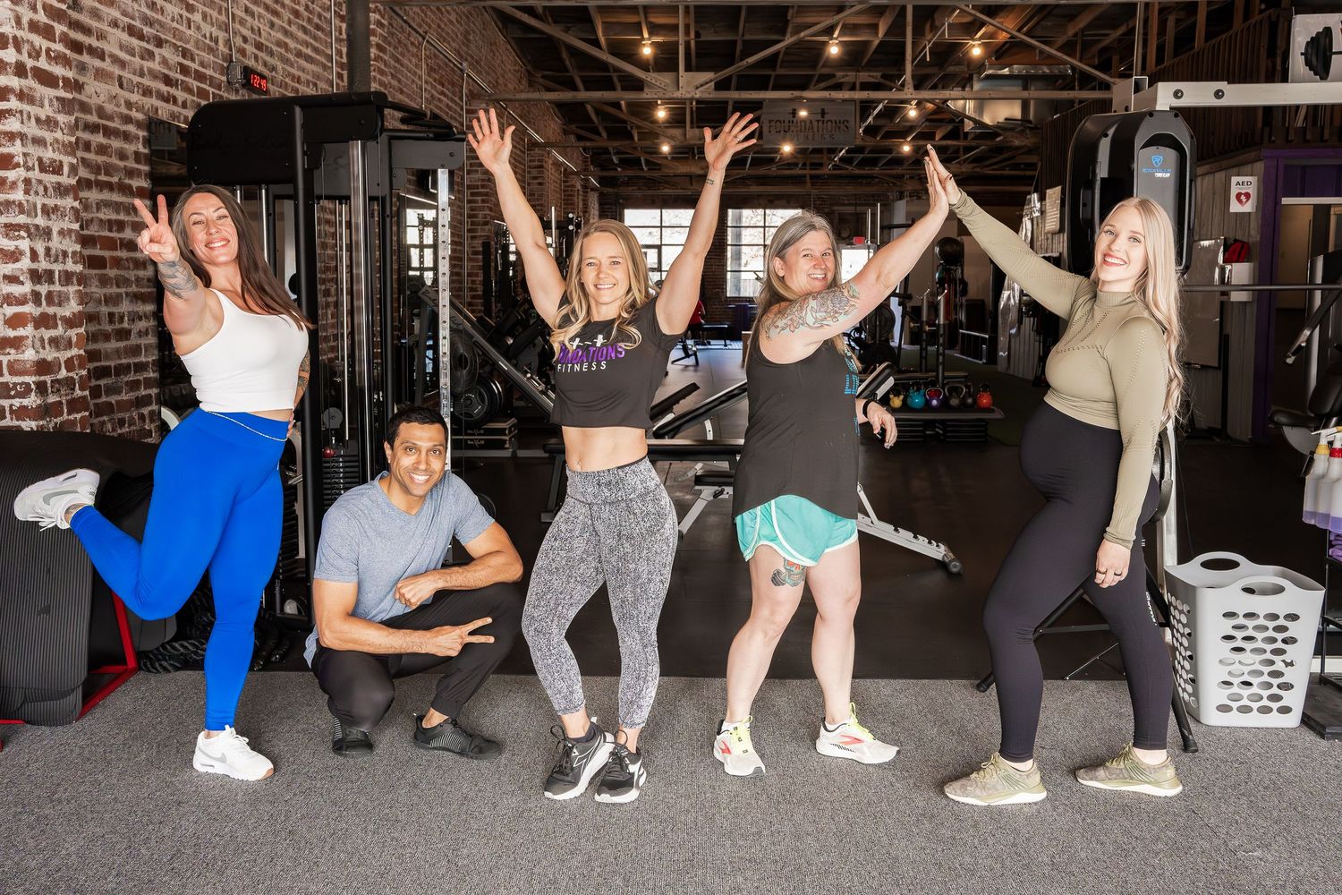 Group of dancers strike dynamic poses against brick wall in dance studio.