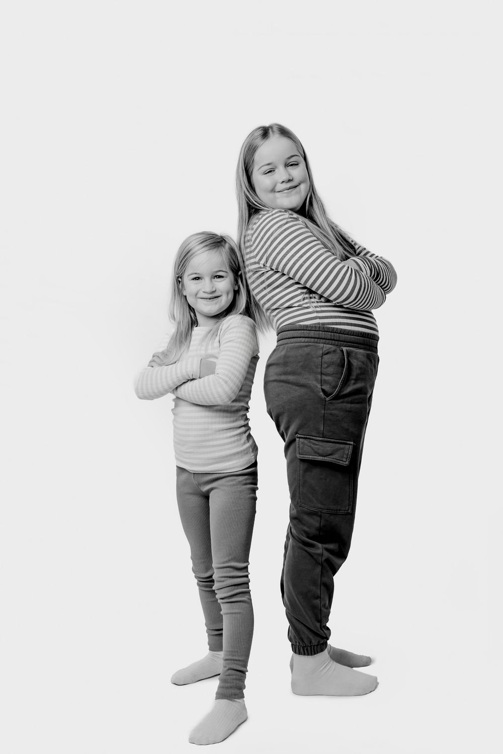 Sort-hvidt portræt af to børn i afslappet tøj, der poserer ryg mod ryg. Børnefotograf Fyn