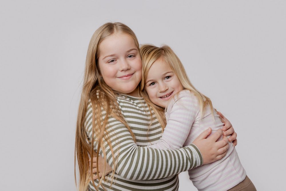 To børn, der deler et kærligt kram og smil foran lys baggrund. Børnefotograf Fyn